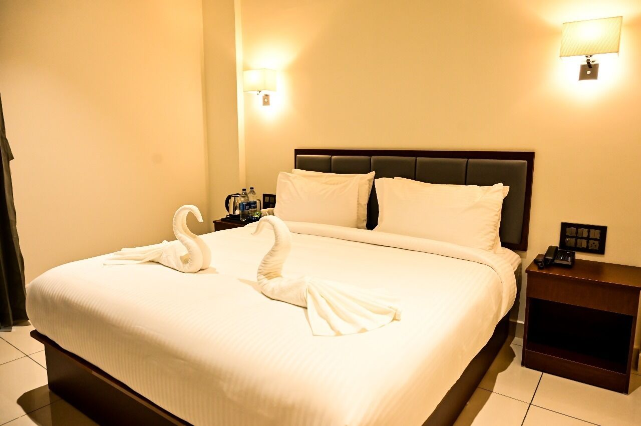 A hotel room with a large bed, two wall-mounted lamps, a nightstand with a phone, and a swan towel arrangement.
