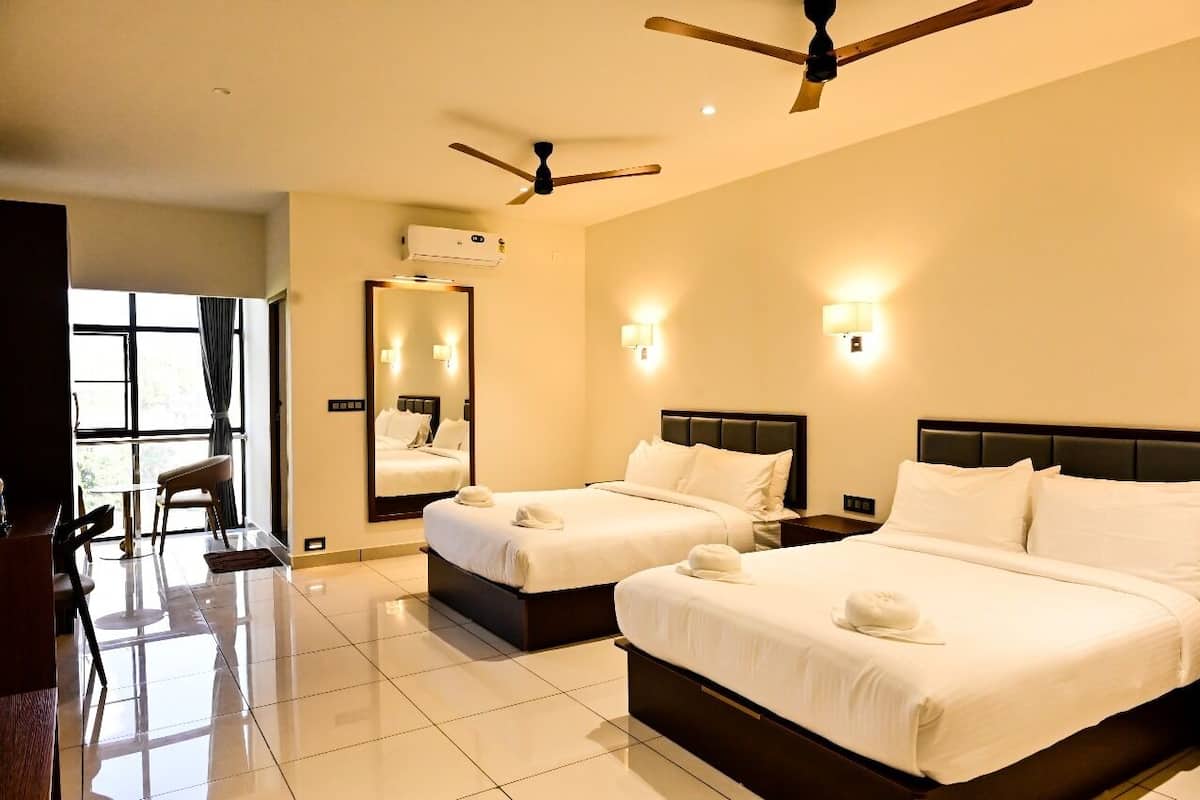 A hotel room with two beds, a ceiling fan, a large mirror, and a seating area with a table and chairs.