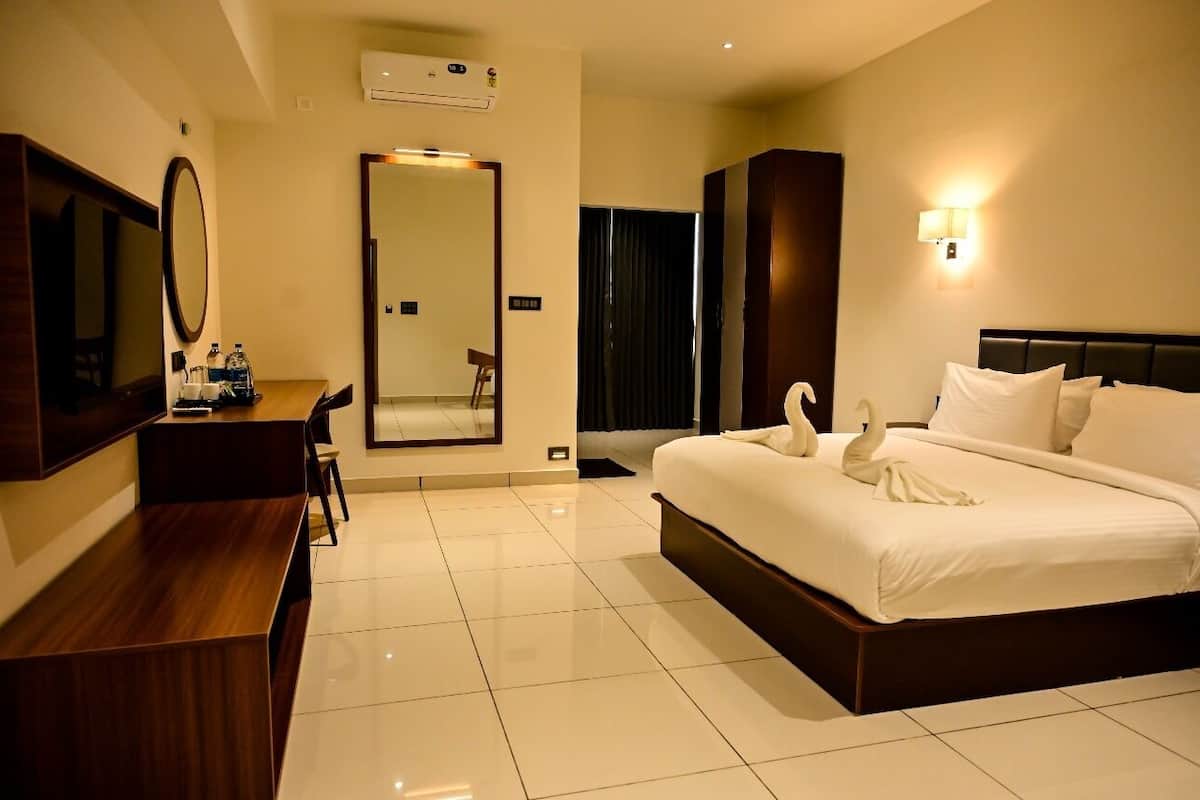 A hotel room with a large bed, a desk with a mirror, a flat-screen TV, and a wall-mounted air conditioner.