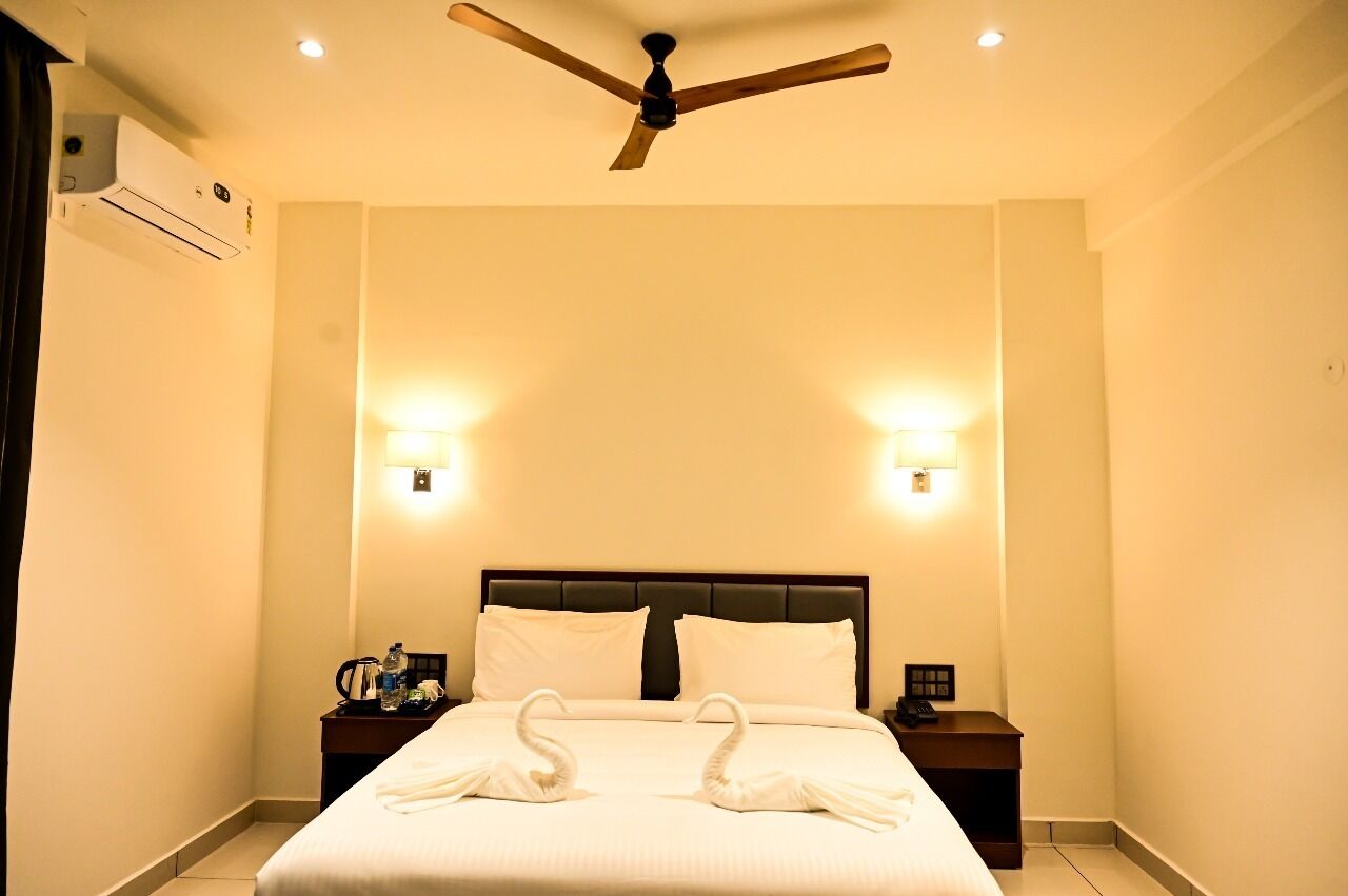 A hotel room with a bed, two wall-mounted lights, a ceiling fan, a nightstand with a phone, and a water bottle.