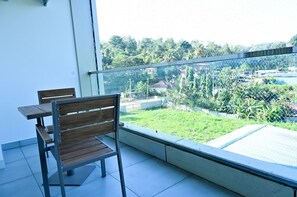 A balcony with a table and chairs, offering a view of a green garden and buildings in the distance. - Hotel S S International (Somvarpet)