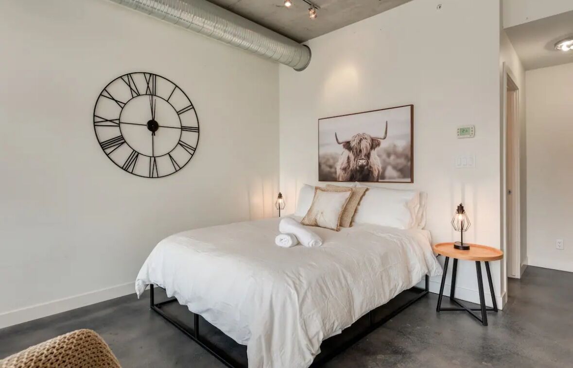 Une chambre moderne avec une grande horloge murale, un tableau encadré représentant un yak et une table de chevet avec une lampe.