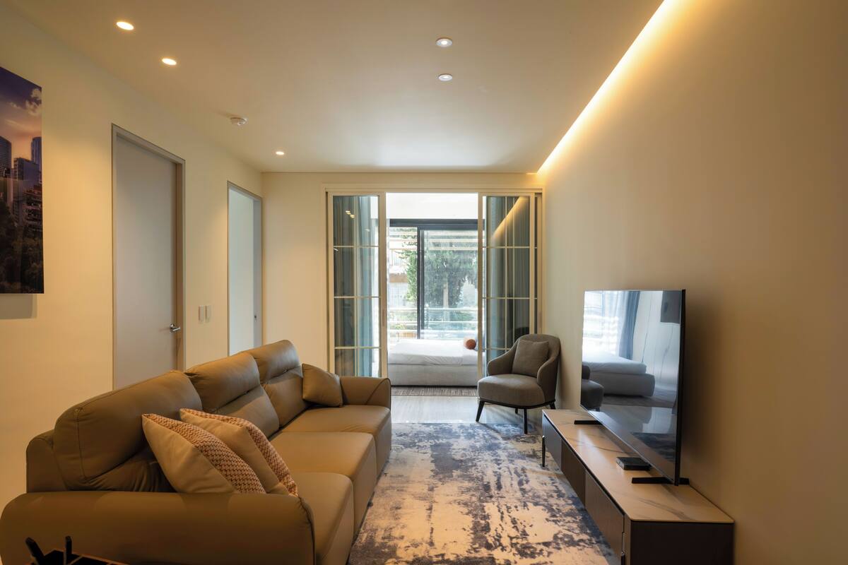 Ein modernes Wohnzimmer mit einer Couch, Sesseln, einem Fernseher und Blick durch Glastüren.