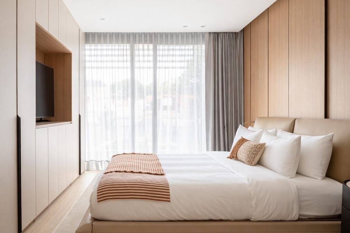 Ein modernes Schlafzimmer mit einem großen Bett, integriertem Fernseher und Blick durch transparente Vorhänge.