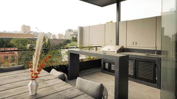 An outdoor patio with a wooden table, a vase with dried plants, and a modern barbecue area.