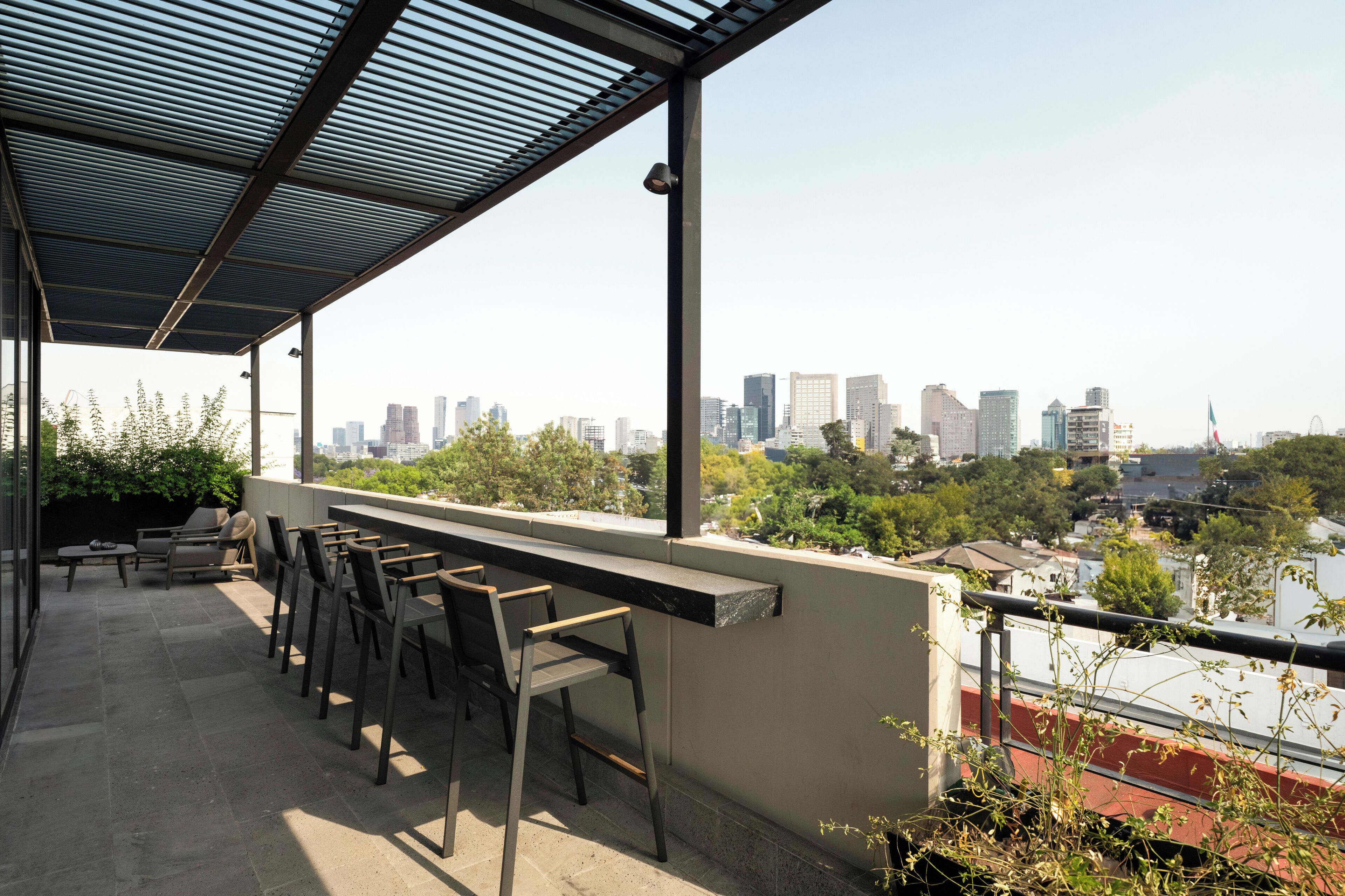 Terraza en la azotea con vistas al horizonte de la ciudad, mobiliario exterior y una estructura de pérgola.