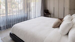 Une chambre moderne avec un grand lit, une chaise et une vue dégagée à travers des rideaux légers.