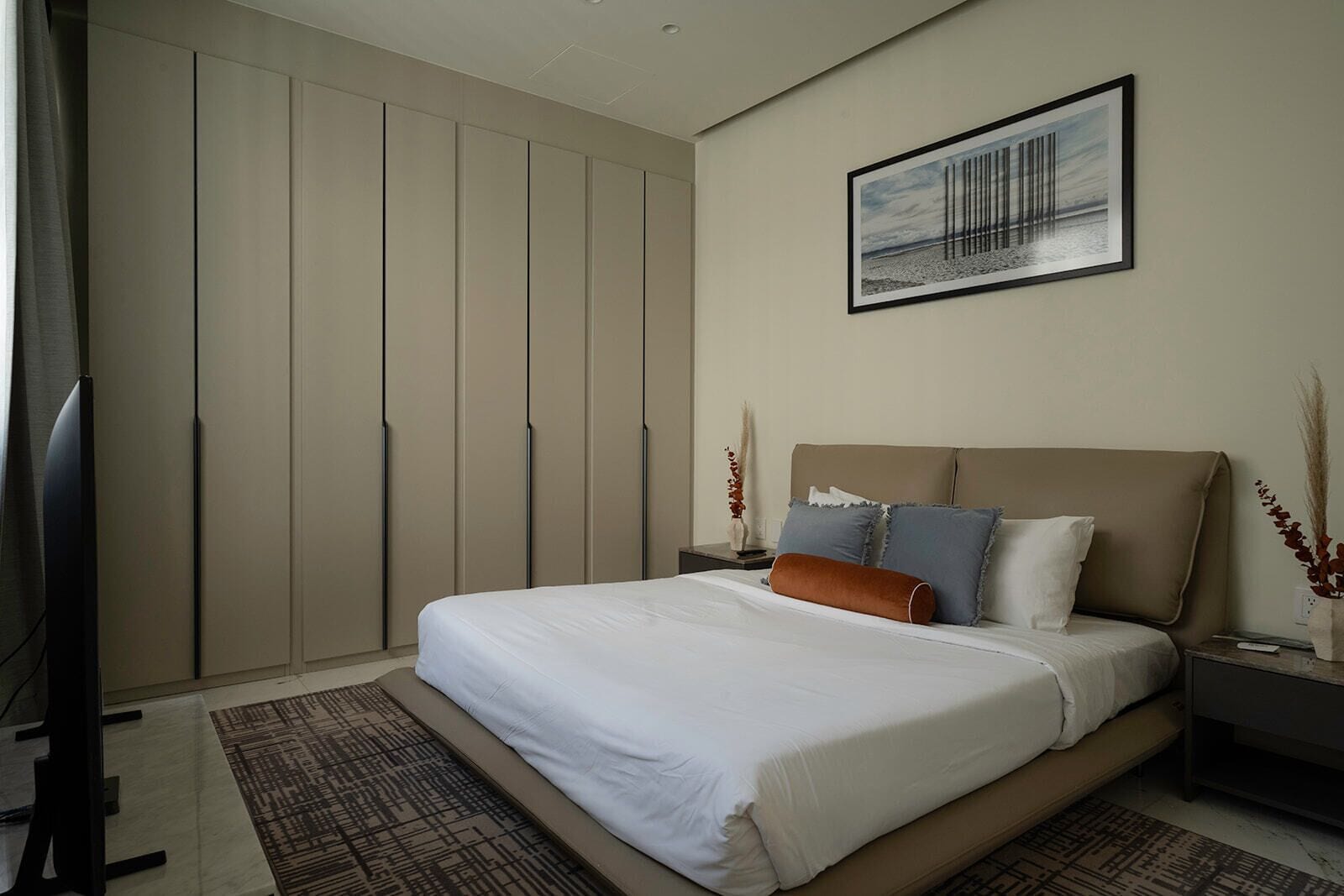 A bedroom with a bed, nightstands, a television, a wardrobe, and a framed picture on the wall.