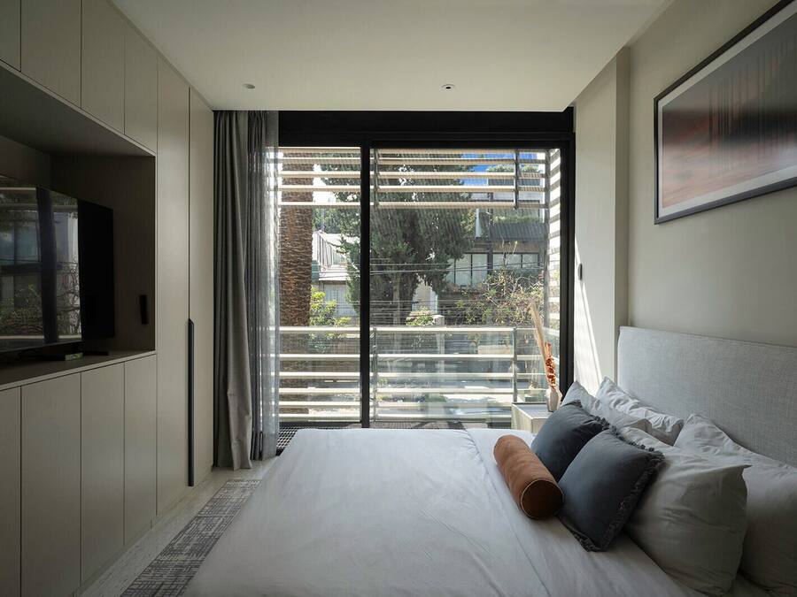 Un dormitorio moderno con una cama grande, televisor de pantalla plana y un balcón con vistas a la ciudad.