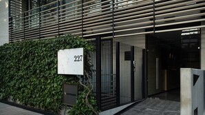Ein moderner Gebäudeeingang mit der Nummer '227', einem Metallgitter und einer Hecke.