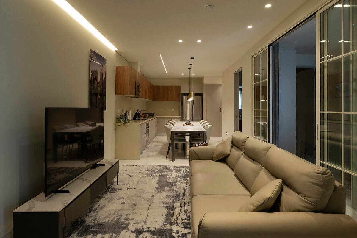 Ein modernes Wohnzimmer mit einem Flachbildfernseher, einem beige farbenen Sofa und einem Essbereich mit Tisch und Stühlen.
