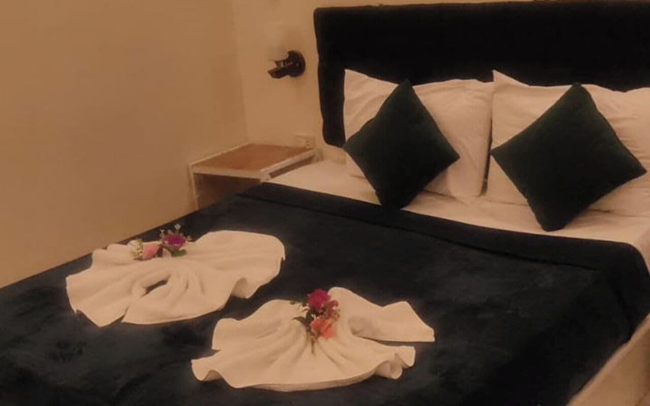A hotel room with a bed, pillows, a nightstand, and a decorative towel arrangement.