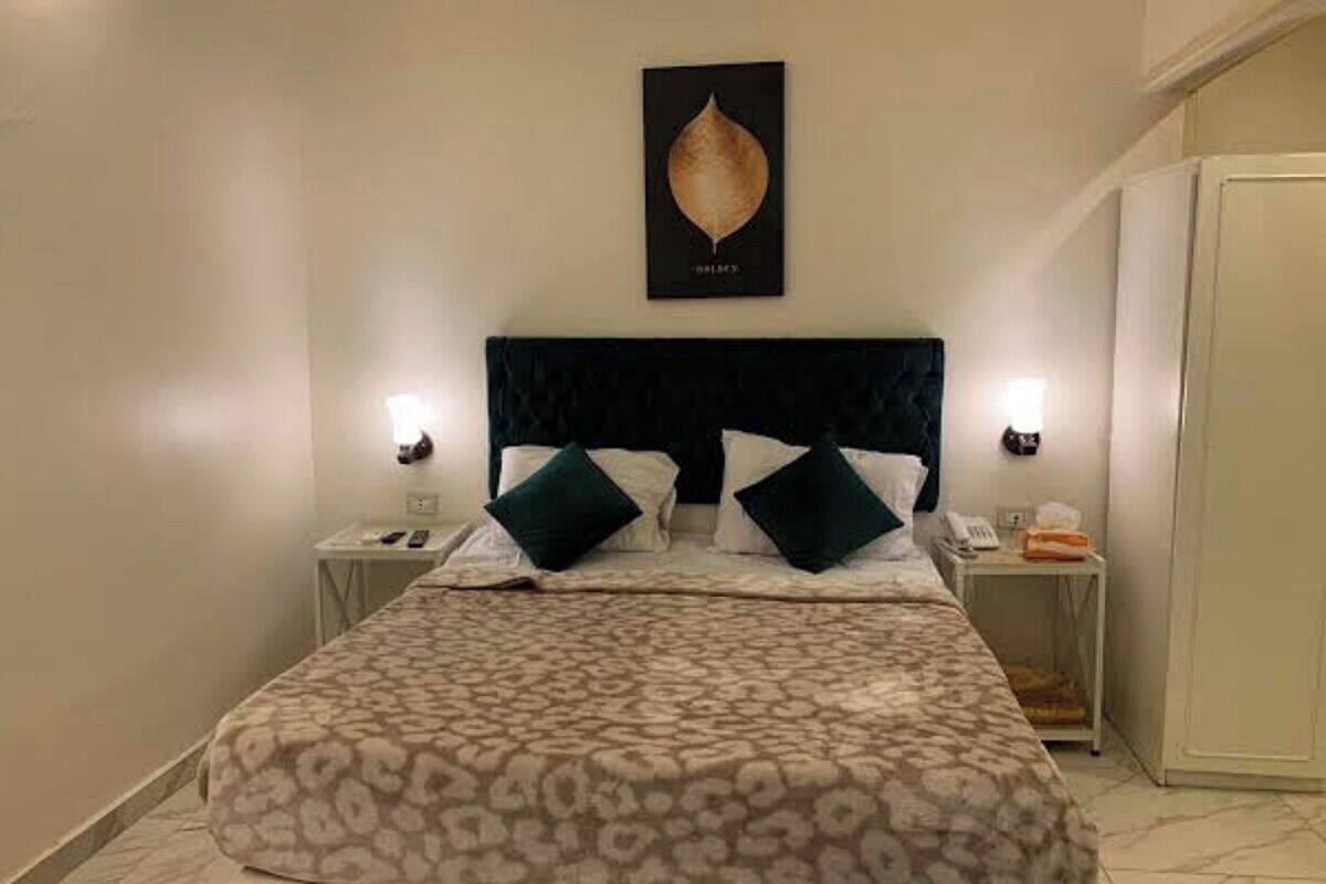 A bedroom with a bed, two bedside tables, a nightstand, a wall-mounted artwork, and a wardrobe.
