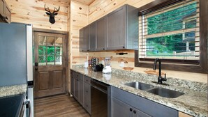 A modern kitchen with granite countertops, stainless steel appliances, and a large window with a view of greenery. - Smoky Ridge Hideaway: Views, Hot Tub, Game Room! (Sevierville)