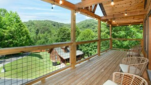 A wooden deck with wicker chairs, overlooking a green landscape. - Smoky Ridge Hideaway: Views, Hot Tub, Game Room! (Sevierville)