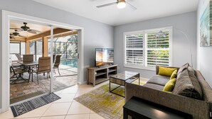 A modern living room with a sofa, coffee table, TV, and dining area with chairs and a table. - Tranquility where relaxation meets coastal charm (Marco Island)