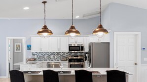 A modern kitchen with white cabinets, a stainless steel refrigerator, and a large island with bar stools. - Tranquility where relaxation meets coastal charm (Marco Island)