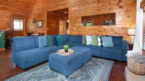 Interior de una cabaña de madera con un sofá seccional azul, una mesita de centro de madera y un tapete estampado.