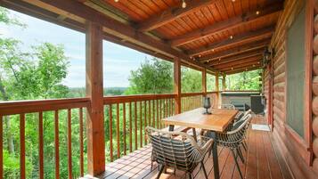 A wooden deck with a table and chairs, overlooking a forested area.