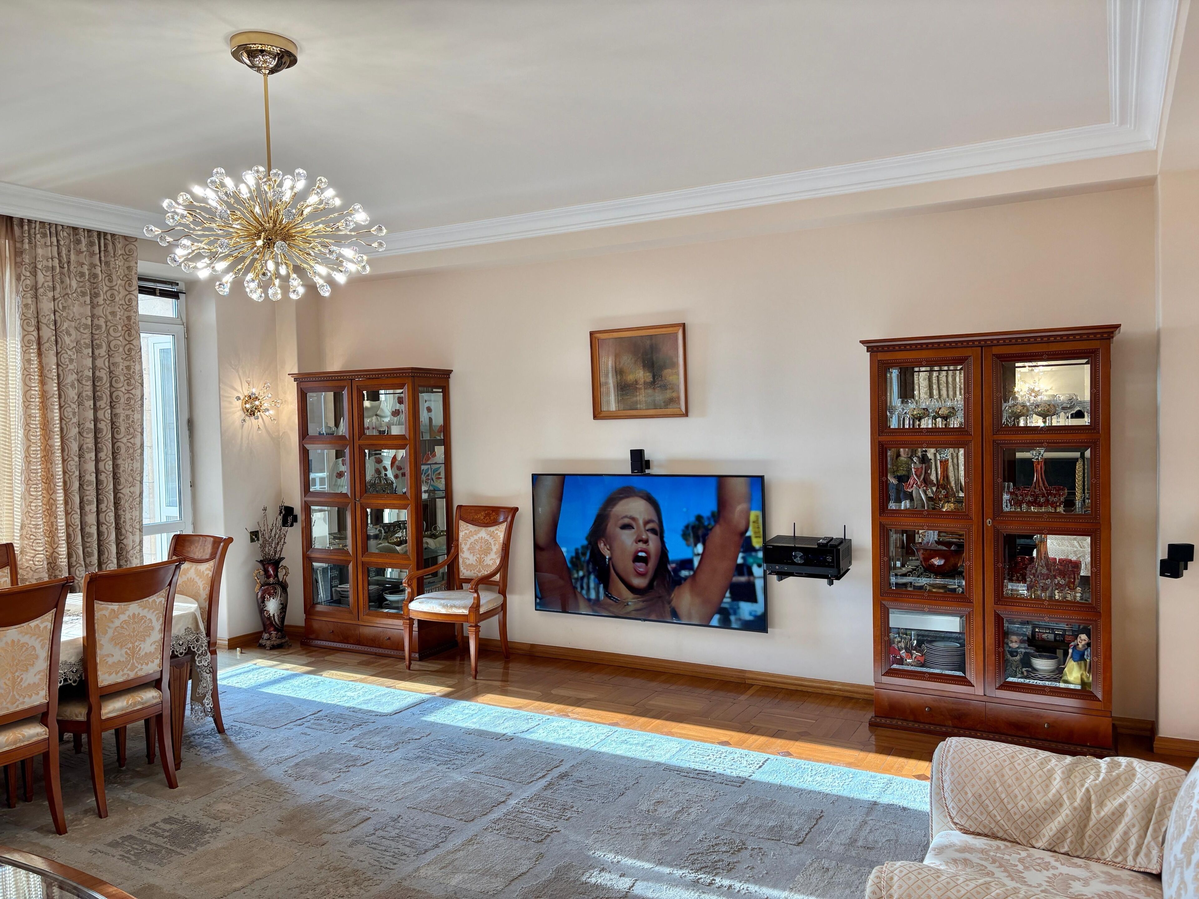 A living room with a television, wooden cabinets, a chandelier, and a dining area.