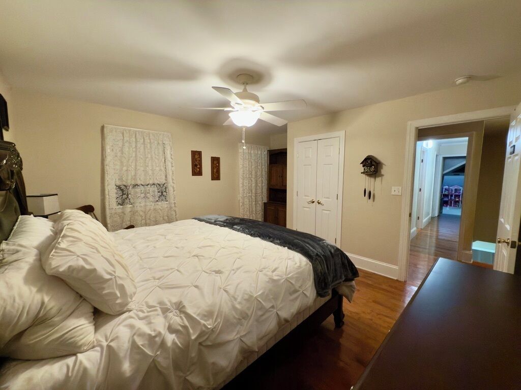 Quarto com cama, ventilador de teto, porta e corredor que dá para outro cômodo.