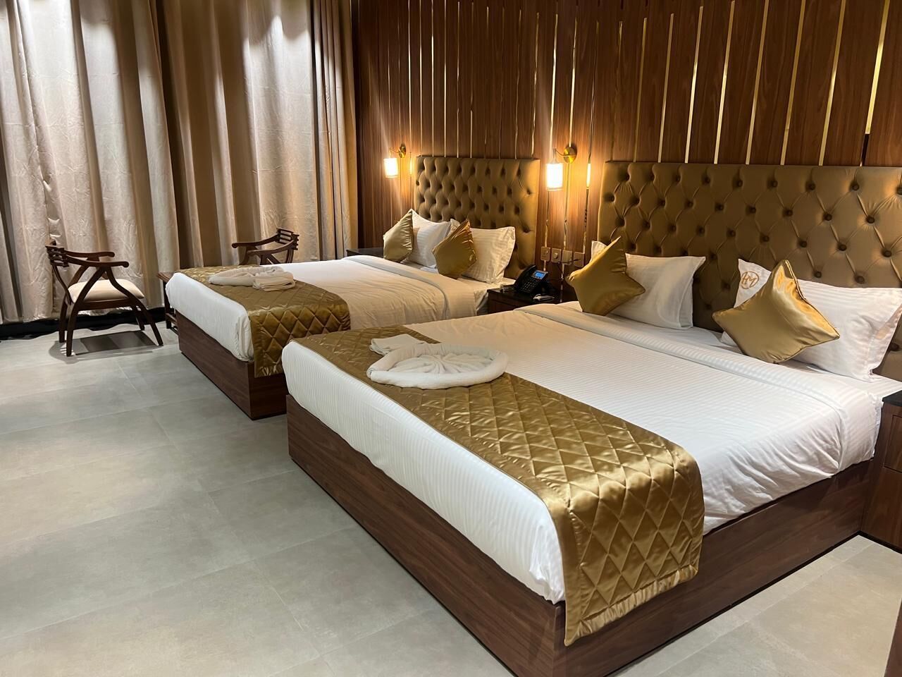 Quarto de hotel com duas camas, cabeceiras de madeira e uma janela grande com cortinas.