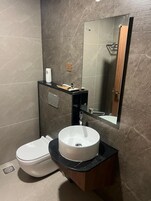 Un baño moderno con inodoro blanco, un lavabo redondo y un espejo encima.