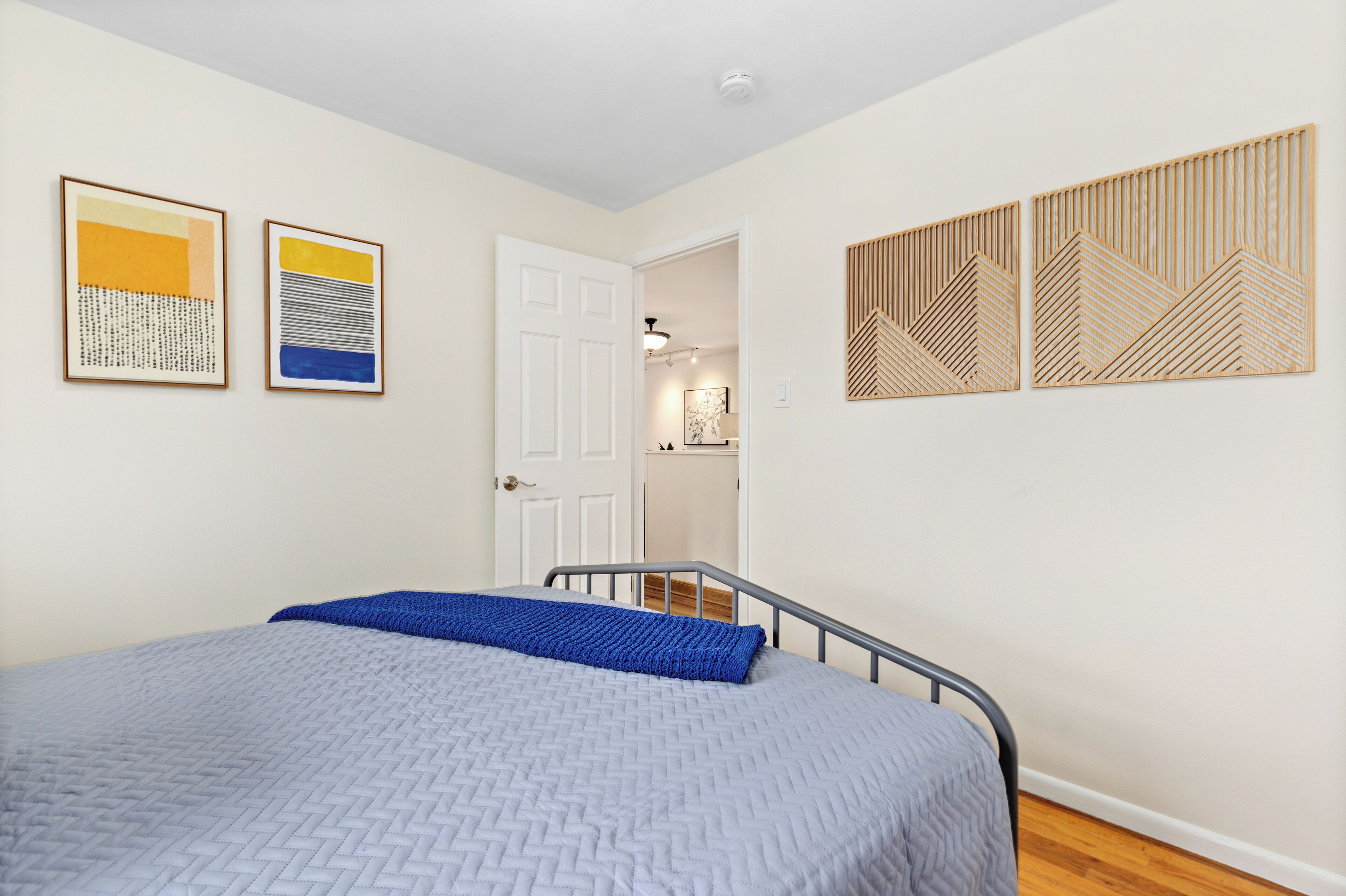 A bedroom with a bed, a door leading to a bathroom, and two framed artworks on the wall.
