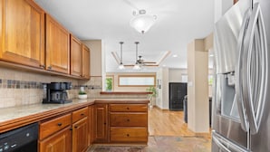 A modern kitchen with wooden cabinets, a stainless steel refrigerator, a dishwasher, and a built-in oven. - Fun House with Pool, Hot Tub, Cool Outdoor Living Space (Centennial)