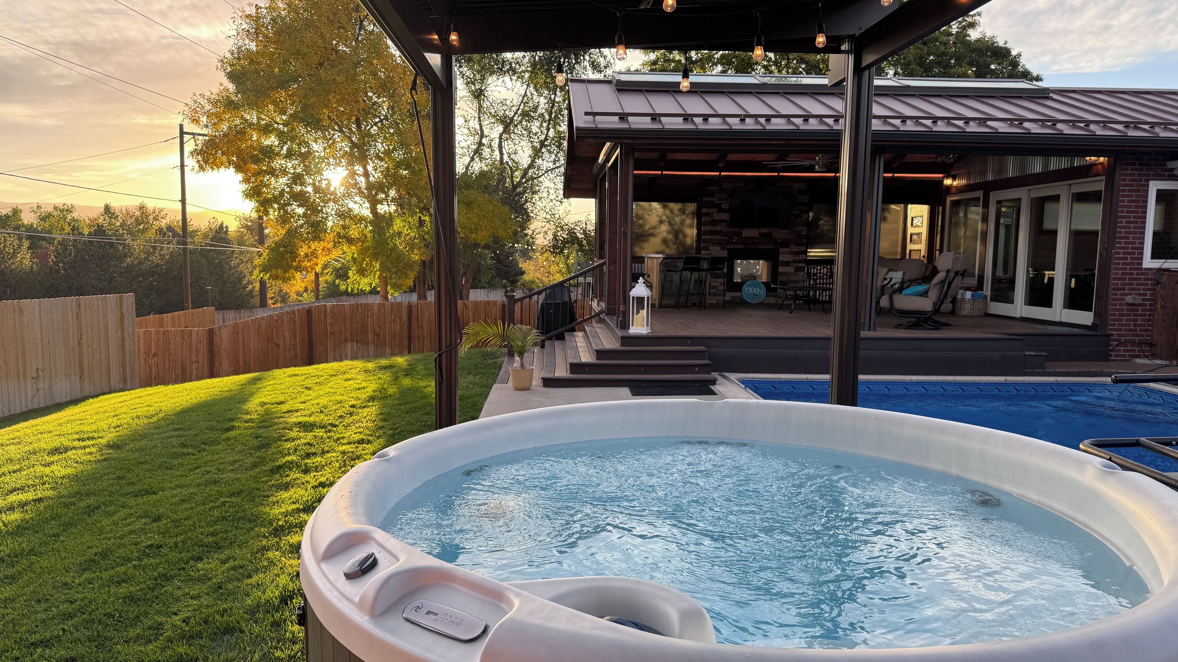 Een jacuzzi in een achtertuin met een overdekt terras, een zwembad en een barbecueplek.