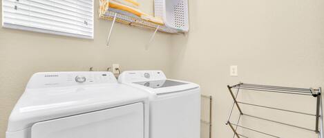 A laundry area with two white Samsung washing machines, a drying rack, and a wall-mounted laundry basket.