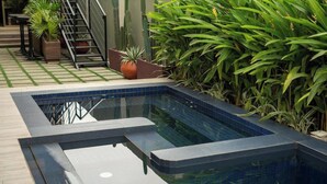 A modern outdoor swimming pool with a tiled edge, surrounded by lush green plants and a wooden deck. - Château NaNa Willine Deluxe Double Room (Accra)