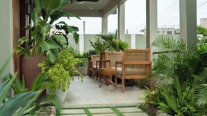 A covered outdoor seating area with wooden chairs and tables, surrounded by various plants and a cactus. - Château NaNa Willine Deluxe Double Room (Accra)