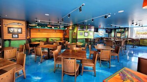 Un restaurante con mesas y sillas de madera, suelo azul y diversas decoraciones en las paredes, incluyendo cuadros enmarcados y un mural.