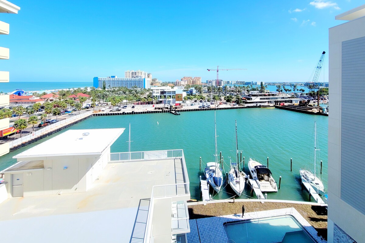 Un puerto deportivo con barcos amarrados, cielo azul despejado y edificios al fondo.