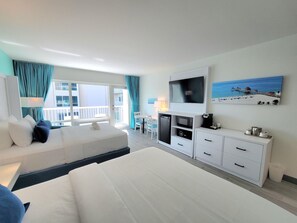 Una habitación de hotel con cama, escritorio, televisión y balcón con cortinas.