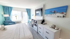 Une chambre d’hôtel équipée d’un lit, d’un bureau, d’une machine à café, d’une télévision et d’un tableau représentant une scène de plage.