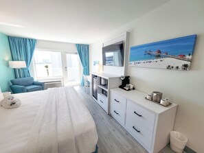 Habitación de hotel con cama, escritorio, cafetera, televisor y un cuadro de una playa.