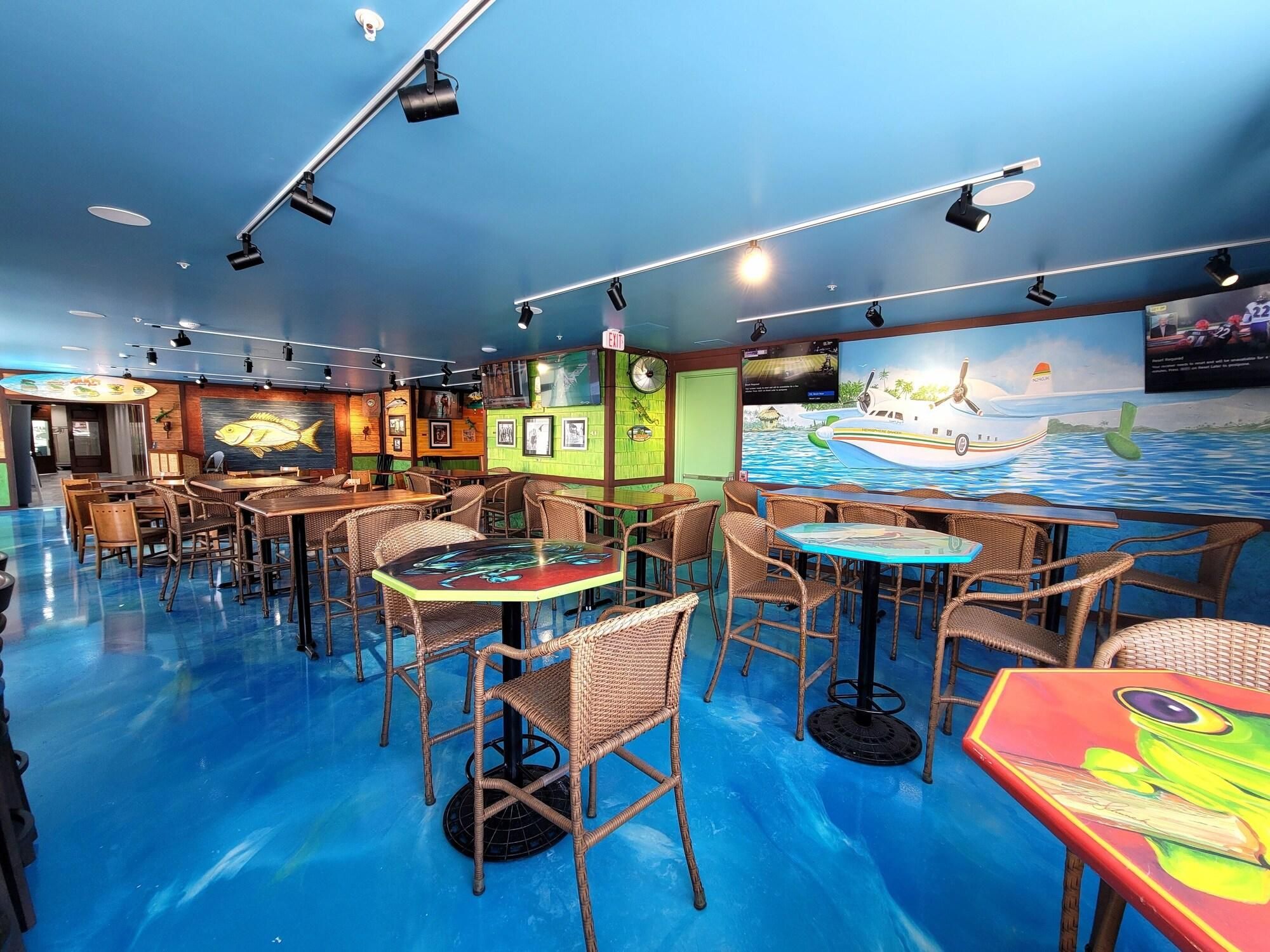 A restaurant with wicker furniture, a blue floor, and a mural of a boat on the wall.
