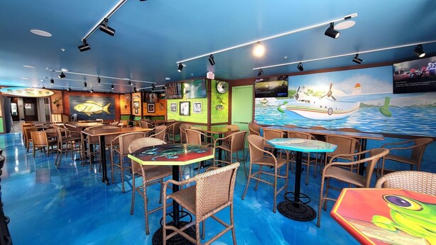 A restaurant with wicker furniture, a blue floor, and a mural of a boat on the wall. - The Chart House Marina Hotel (Clearwater Beach)