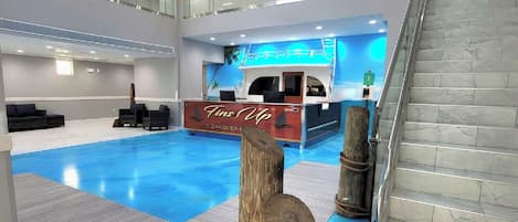 A modern hotel lobby with a pool, a reception desk, and a staircase.