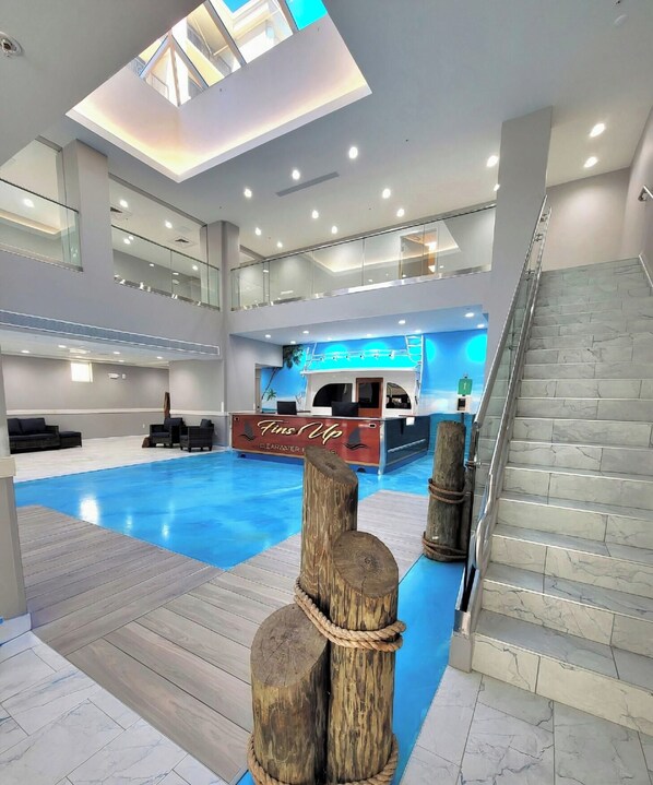Un moderno vestíbulo de hotel con piscina, mostrador de recepción y una escalera.