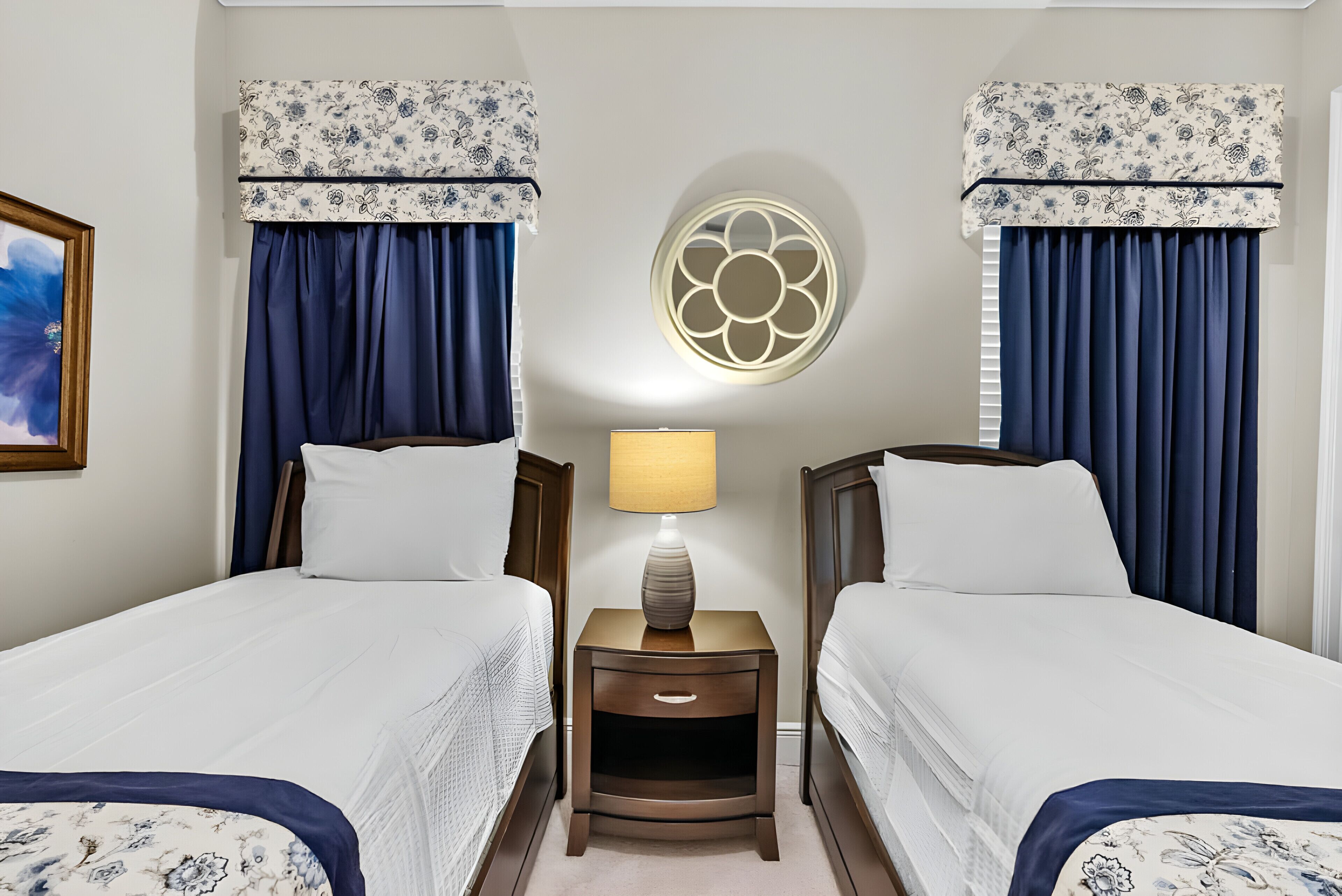 Habitación de hotel con dos camas, una mesita de noche con lámpara y un adorno en la pared.