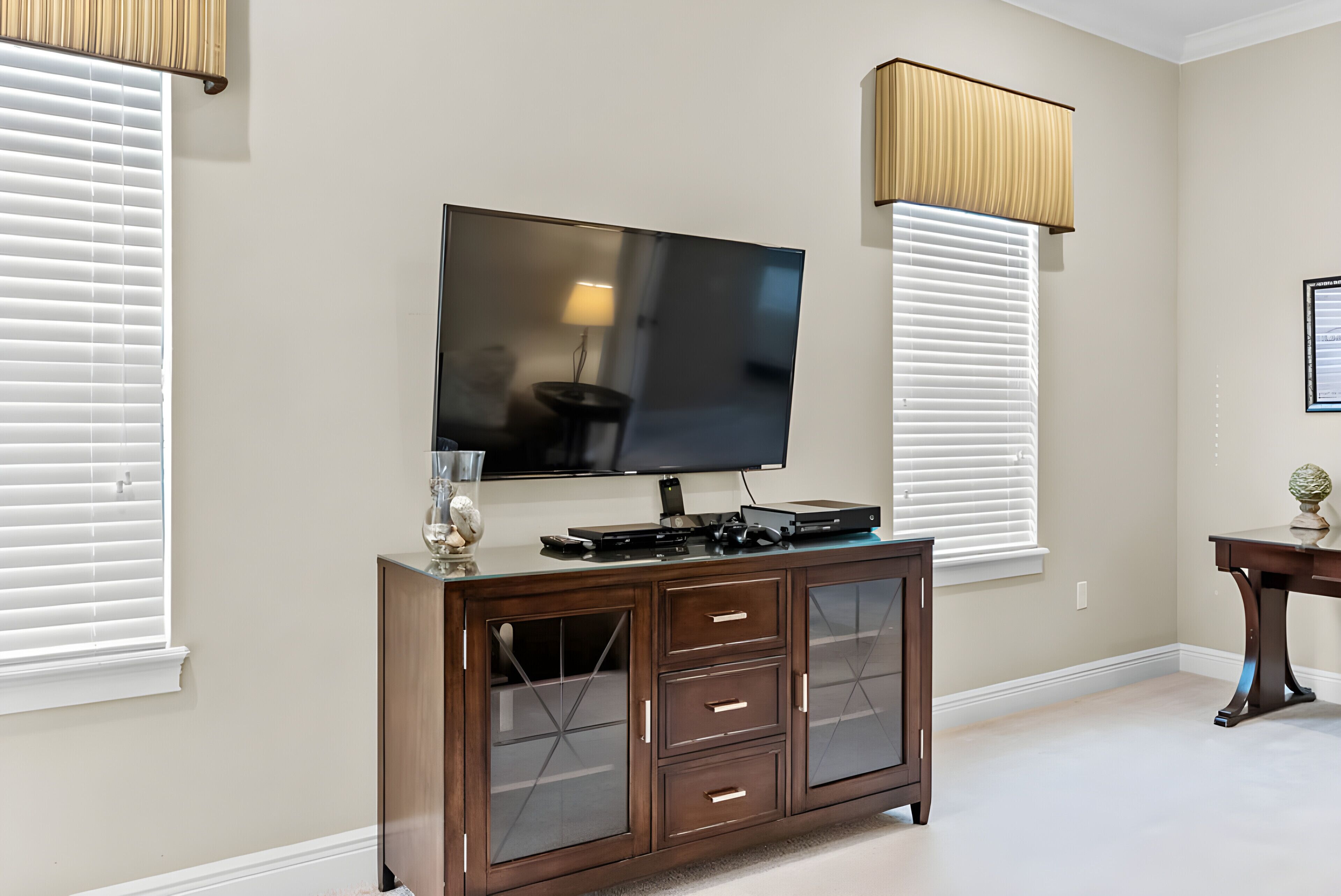A living room with a flat-screen TV mounted on the wall, a wooden cabinet with drawers, and a table with a lamp.