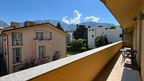 Een balkon met een gele muur, uitzicht op omliggende gebouwen en een berg op de achtergrond.