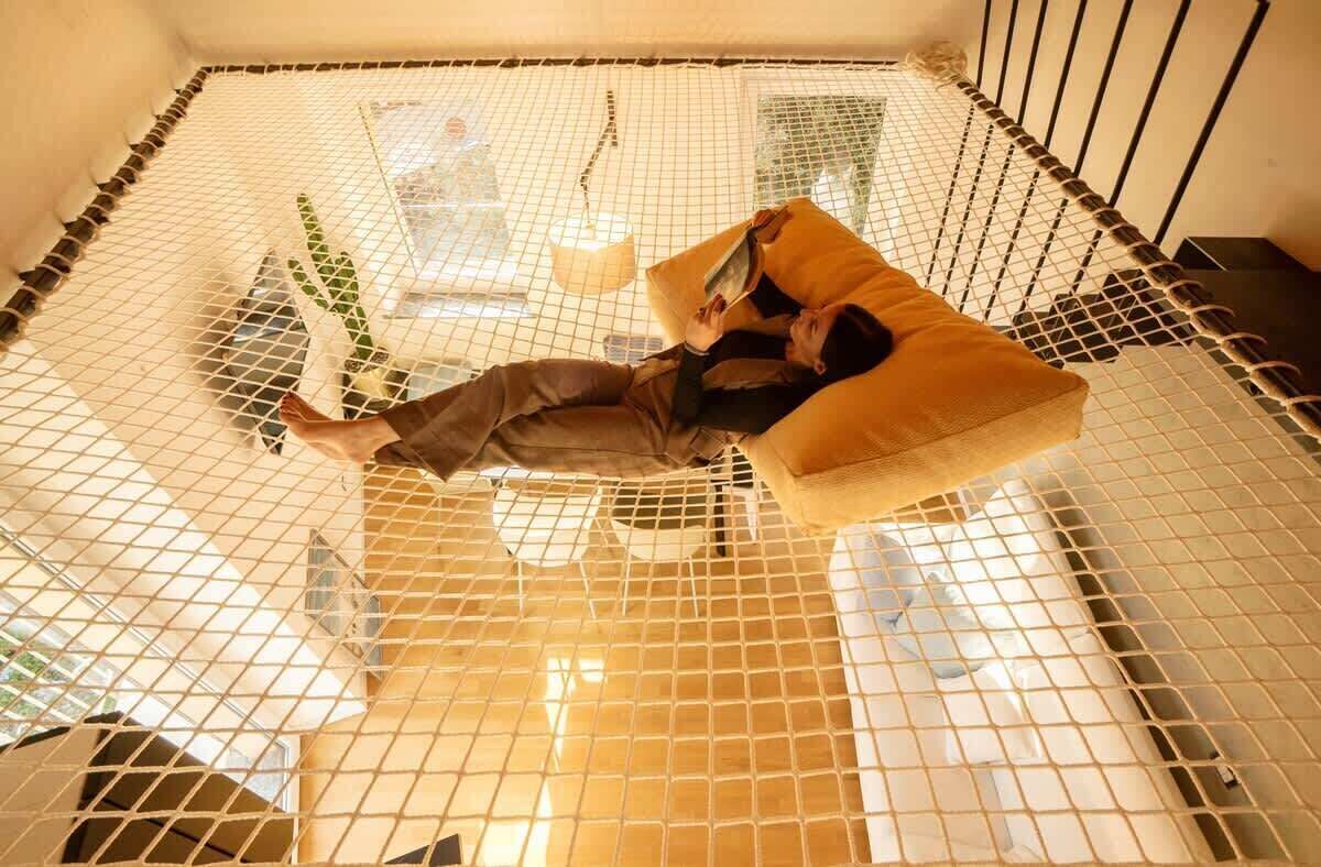 Eine Person liegt in einer Hängematte in einem Raum mit Netzdecke, Fenster und Pflanze.