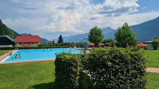 A swimming pool surrounded by greenery and mountains in the background.