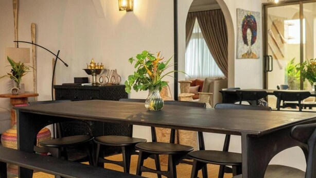 A modern dining area with a dark wooden table and black chairs, a vase with green plants, and a decorative lamp. - Château NaNa Willine Deluxe Double Room F (Accra)