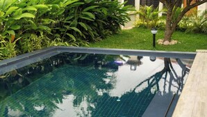 A rectangular swimming pool with clear water, surrounded by a wooden deck and lush greenery. - Château NaNa Willine Deluxe Double Room H (Accra)
