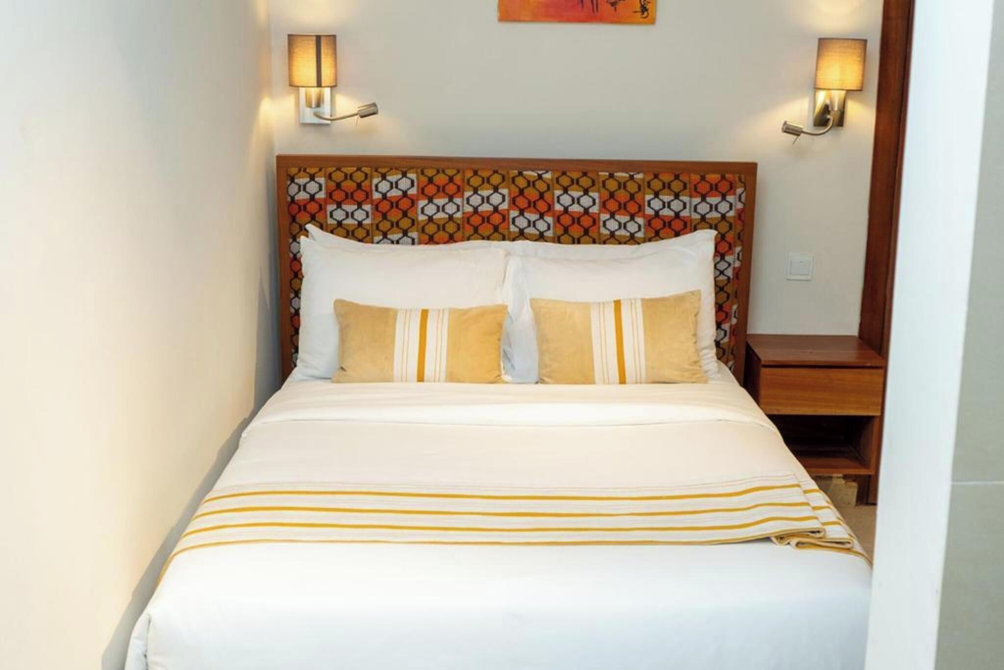 A neatly made bed with a patterned headboard, two bedside lamps, and a wooden nightstand.